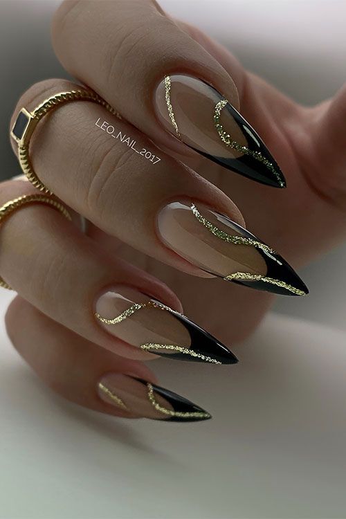 Elegant Stiletto Nail Design: Black Tips, Transparent Bases, and Glamorous Gold Glitter Accents.