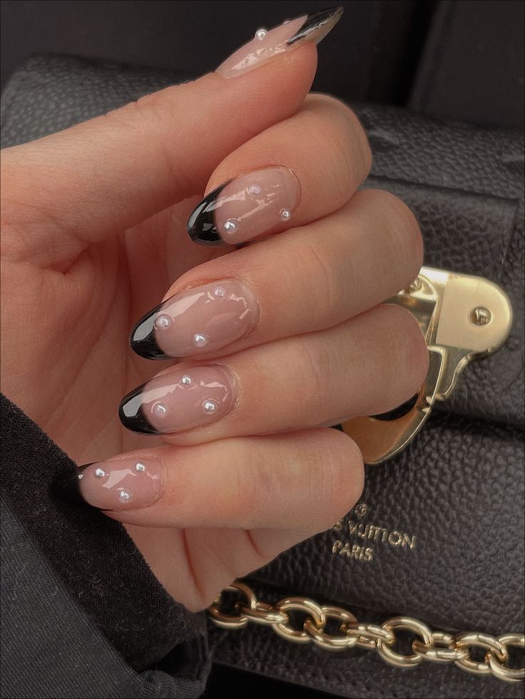 Chic Nail Design: Delicate Nude Base with Bold Black Tips and Glamorous Silver Studs.