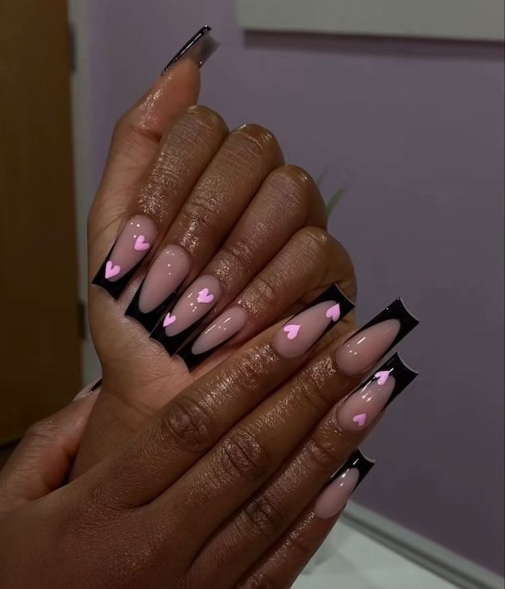 Chic Almond-Shaped Nails with Glossy Nude Base, Bold Black Tips, and Playful Pink Hearts.