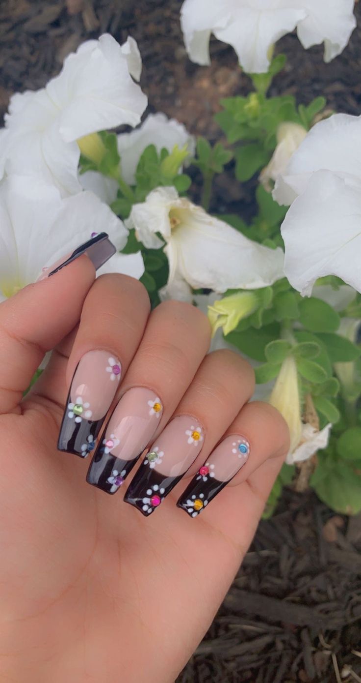 Chic Nude and Black French Tip Nail Design with Vibrant Floral Embellishments.