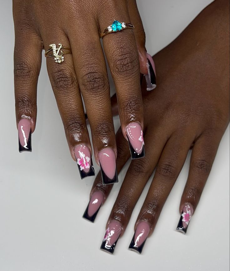 Sophisticated Soft Pink and Bold Black Nail Design with Floral Accents and Elegant Ring Pairings.