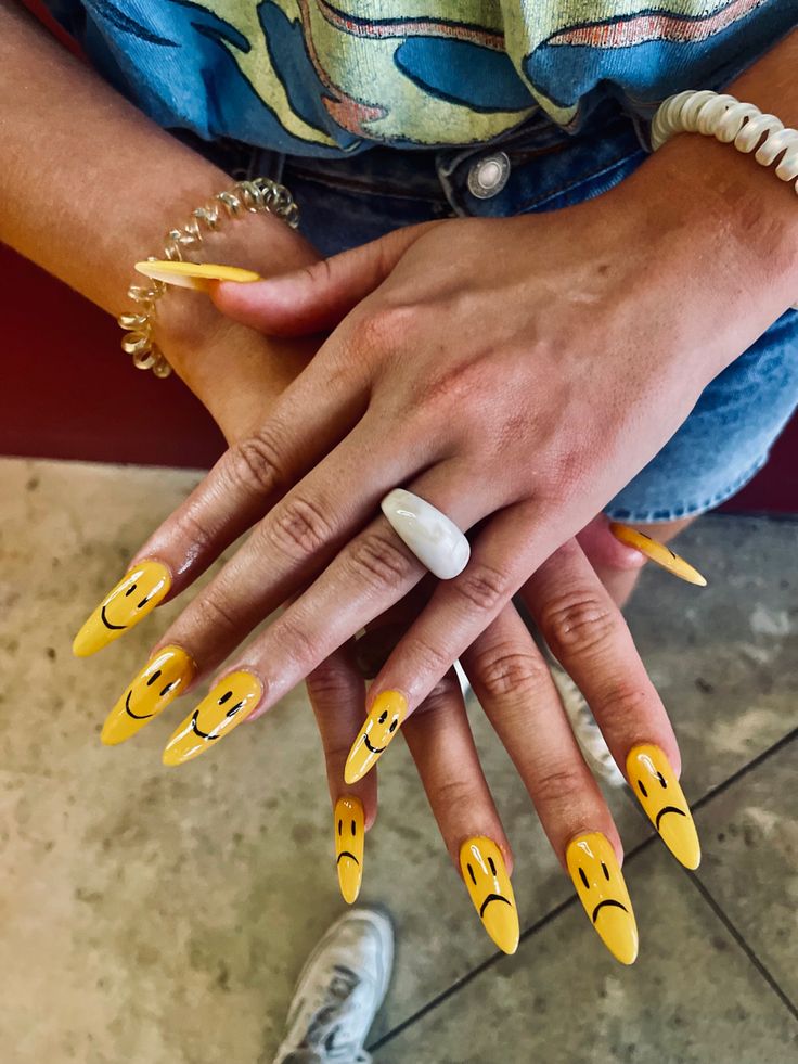 Playful Whimsical Yellow Nail Design with Smiley Faces and Dramatic Stiletto Shapes.