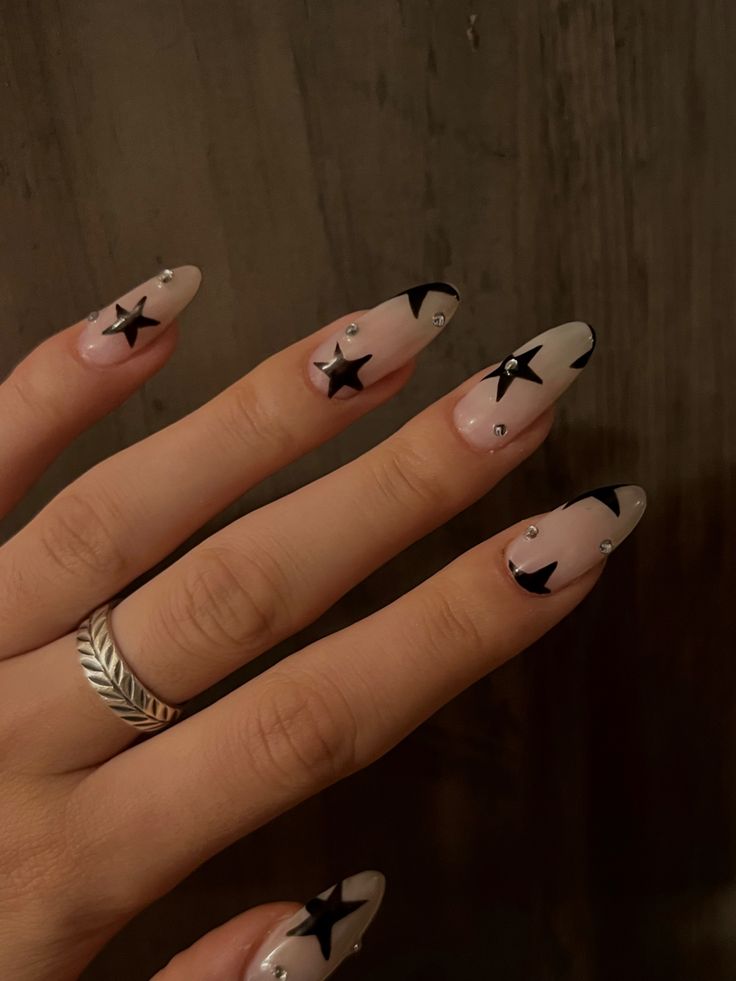 Chic Almond-Shaped Nude Nails with Bold Black Stars and Sparkling Rhinestones.