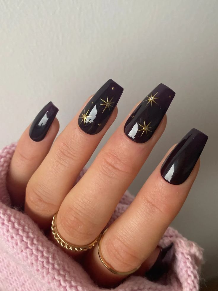 Chic Nighttime Nail Design: Deep Purple Polish with Gold Star Accents and Textured Finishes.