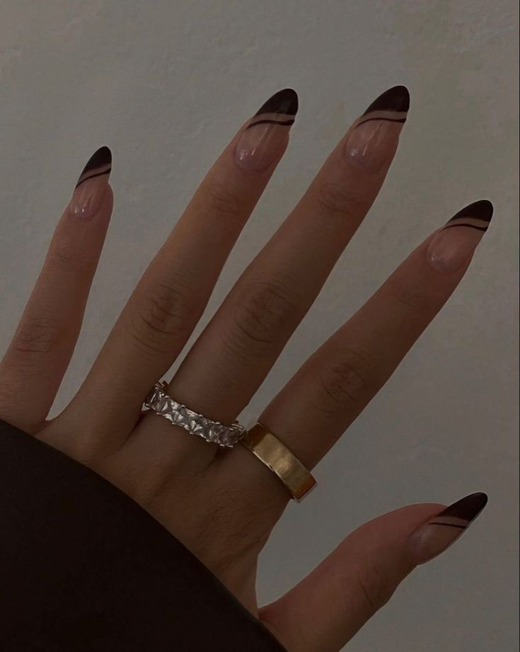 Chic Nude Almond-Shaped Nail Design Accented with Bold Black Lines and Delicate Rings.