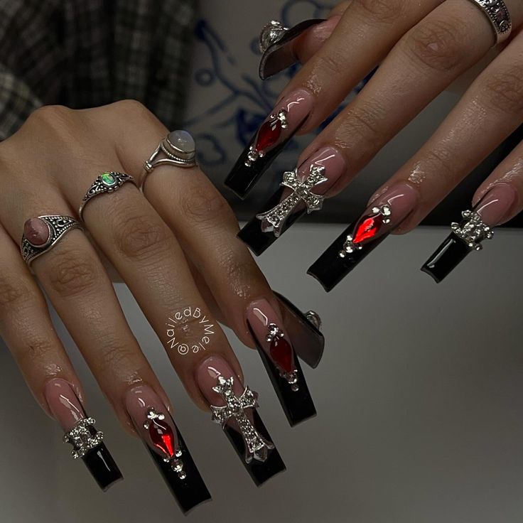 Dramatic Long Rectangular Nail Design: Black and Nude with Silver Cross Charms and Red Gemstones.