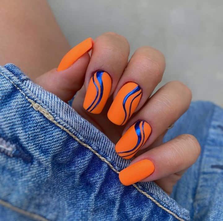 Bold Matte Orange Nails with Artistic Blue Waves for a Trendy Statement Look.