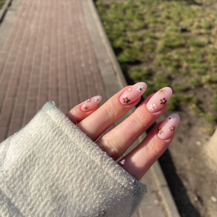 Charming Floral Nail Design: Soft Pink Ombre with Delicate White and Brown Accents.