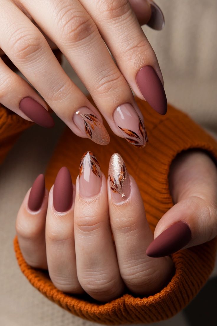 Chic Elegance: Deep Burgundy and Nude Nail Design with Leaf Motifs and Gold Accents.