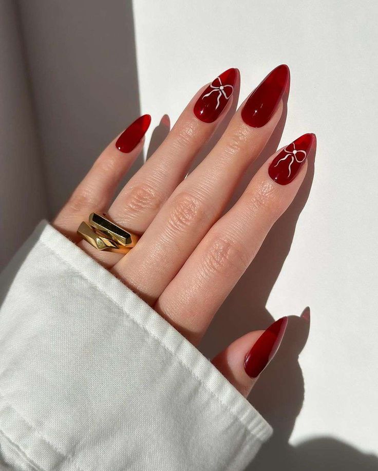 Sophisticated Almond-Shaped Red Nail Design with Delicate White Accents and Bold Gold Ring.