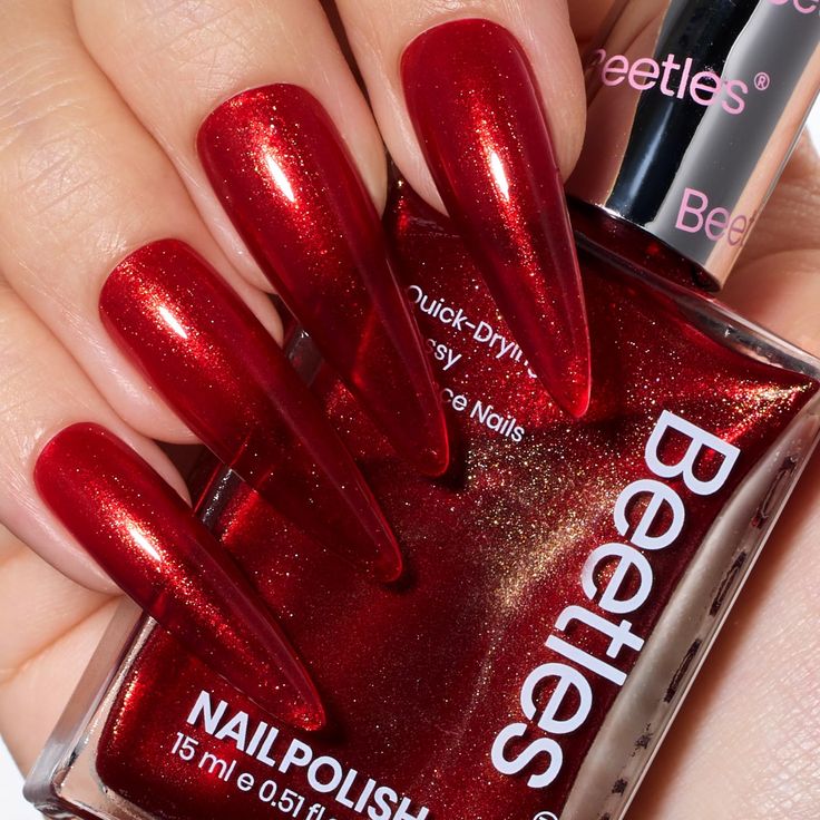 Luxurious Deep Red Stiletto Nails with Shimmering Gold Flecks for a Glamorous Manicure.