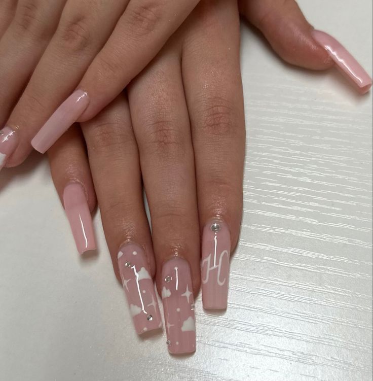 Sophisticated Soft Pink Nail Design with Artistic White Accents and Glamorous Rhinestones.