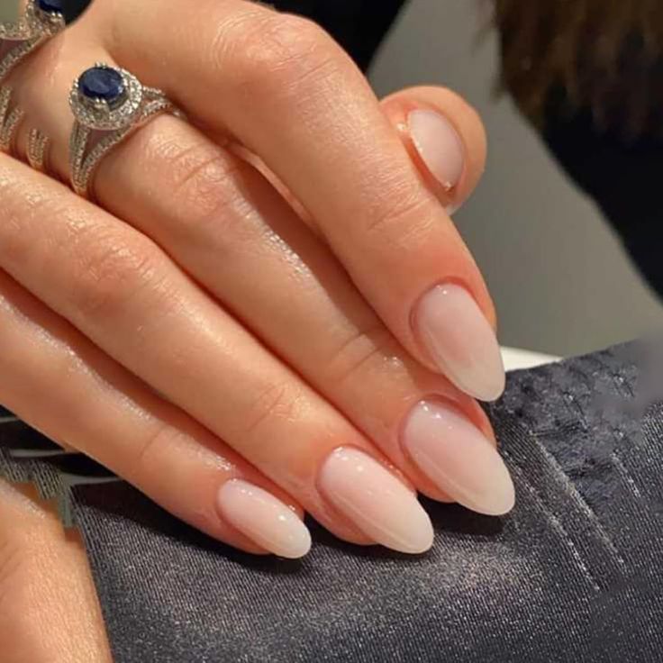 Sophisticated Almond-Shaped Ombre Nails in Soft Nude and Light Pink, Accentuated by Delicate Rings.