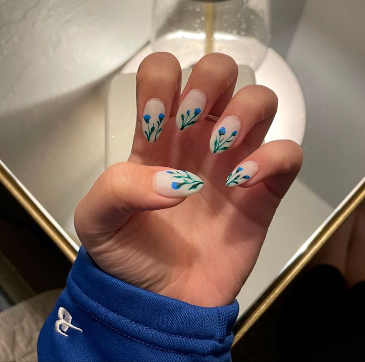 Elegant Floral Nail Design with Delicate Blue Flowers and Green Leaves on a Soft White Base.