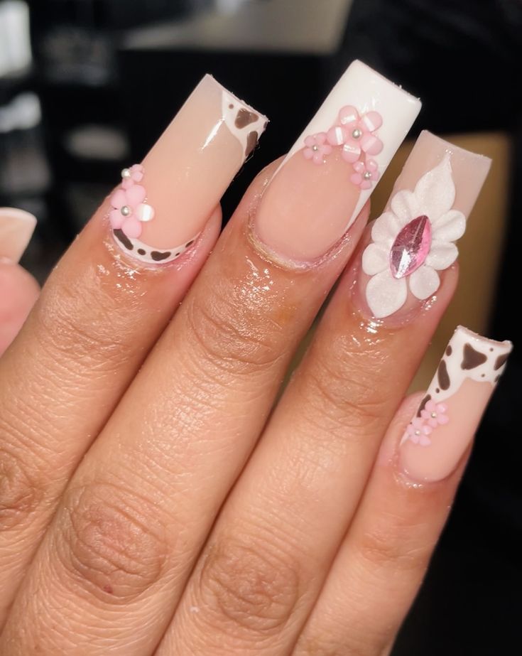 Playful Pastel Pink Cow-Print Nail Design With Floral Accents and Gemstone Elegance.