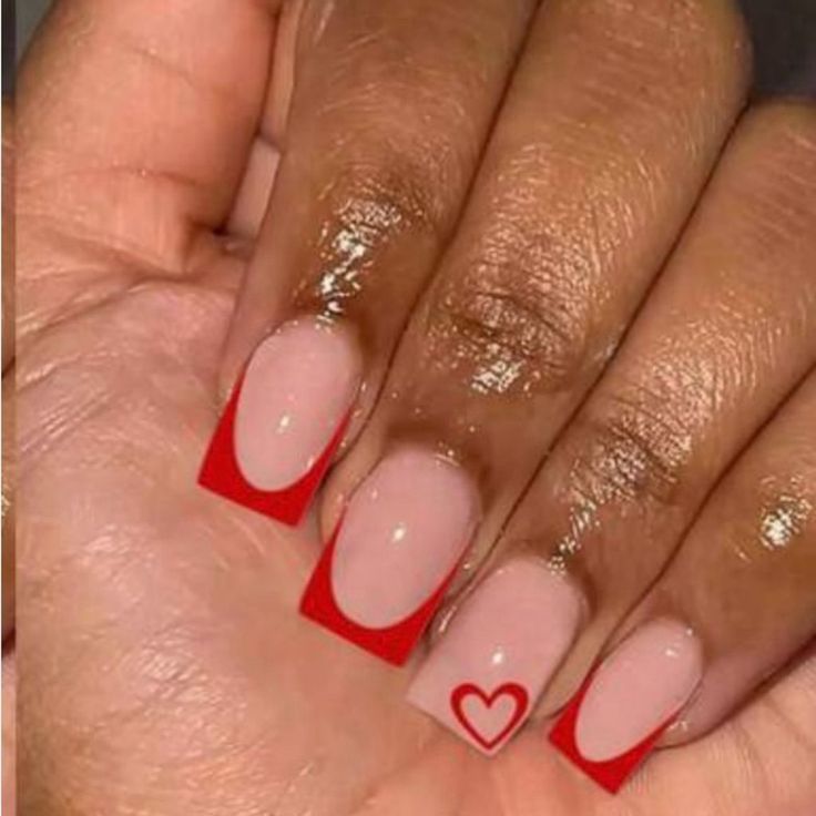 Romantic Nail Design: Soft Nude Base with Bold Red Tips and Playful Heart Accent.