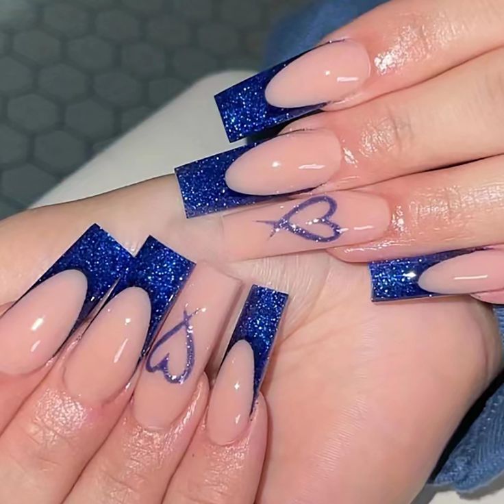 Chic Deep Blue Glitter Tip Nail Design with Heart Accents on Elegant Nude Base.