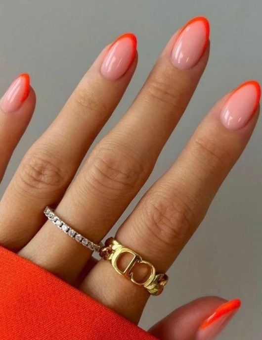 Chic Almond-Shaped Nail Design with Nude Pink and Vibrant Orange Tips, Enhanced by Glamorous Rings.