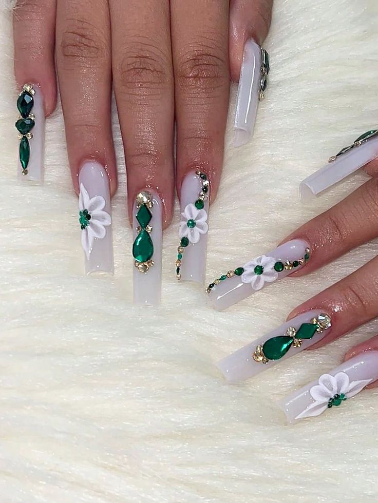 Sophisticated Floral Nail Design with Intricate White Flowers and Sparkling Green Gemstones on Nude Acrylic Base