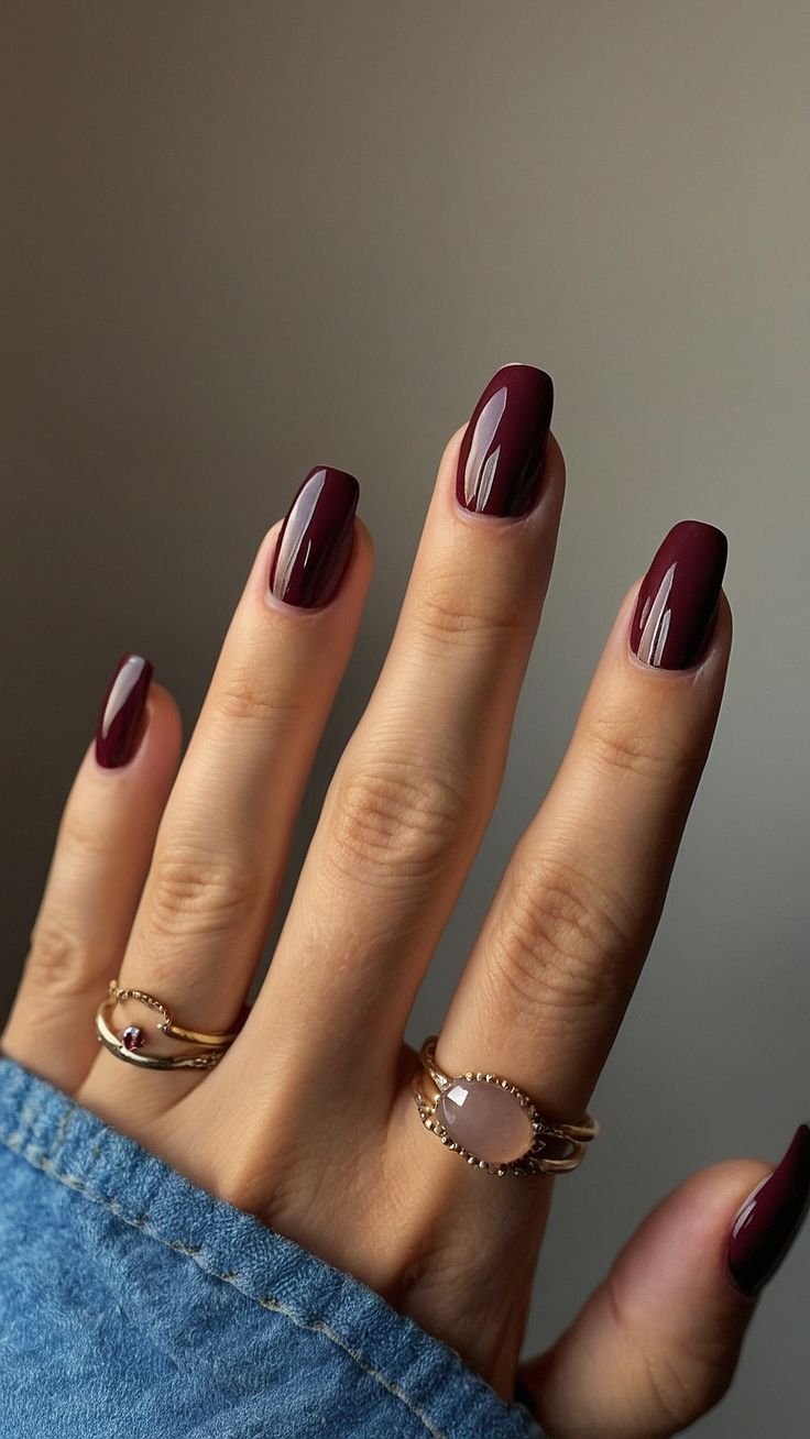 Sophisticated Burgundy Nail Design with Glossy Finish and Gold Ring Accents.