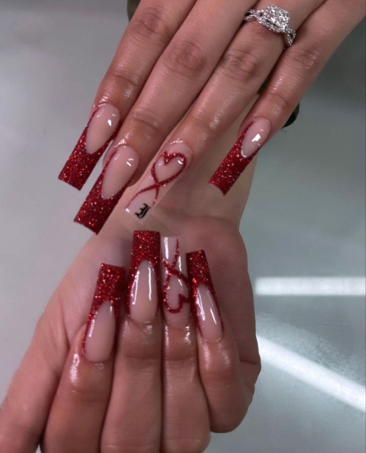 Bold Glittering Red and Nude Nail Design with Intricate Heart Patterns and Glossy Finish.