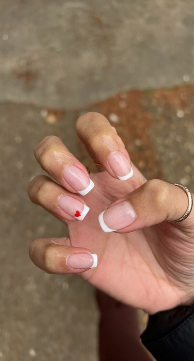 Chic French Tip Manicure with a Playful Red Heart Accent.