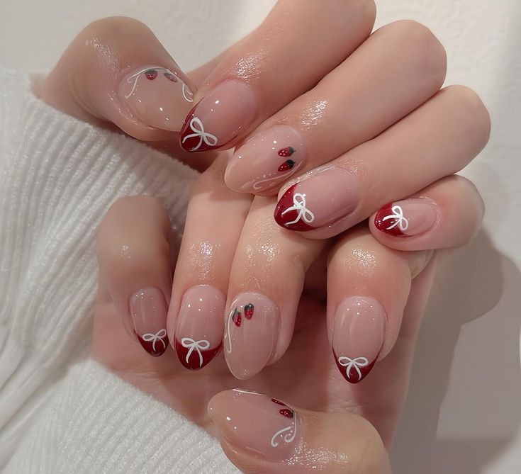 Elegant Nail Design: Glossy Nude and Deep Red with Delicate Bows and Embellishments.