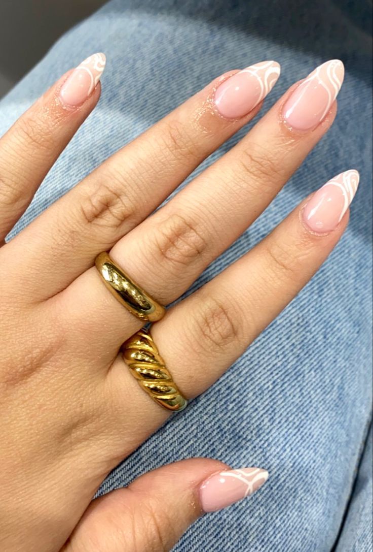 Chic Soft Pink Nail Design with Delicate White Swirls and Bold Gold Rings.