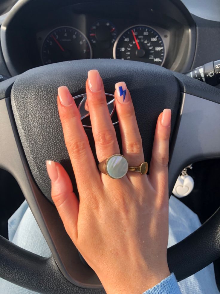 Chic Nude Nail Design with Striking Blue Lightning Bolt Accent and Statement Rings.