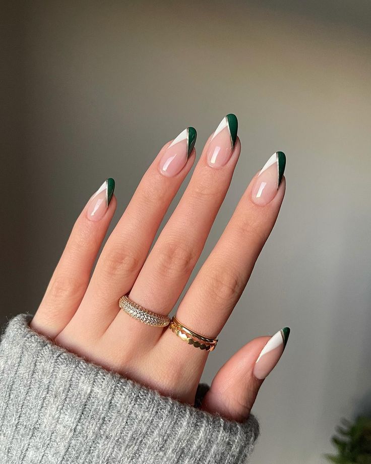 Elegant Nail Design: Almond Tips with Dark Green and White Geometric Patterns on a Nude Base, Complemented by Delicate Rings and a Cozy Sweater.