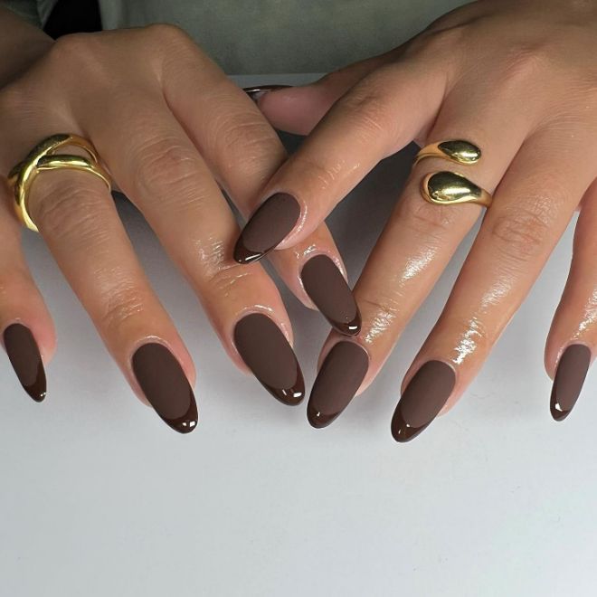 Elegant Almond-Shaped Brown Nails with Glossy Finish and Dark Chocolate Tips Adorned by Minimalist Gold Rings.