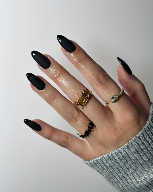 Chic Contrast: Glossy Black Almond Nails and Sophisticated Gold Rings Paired with a Cozy Grey Sweater.