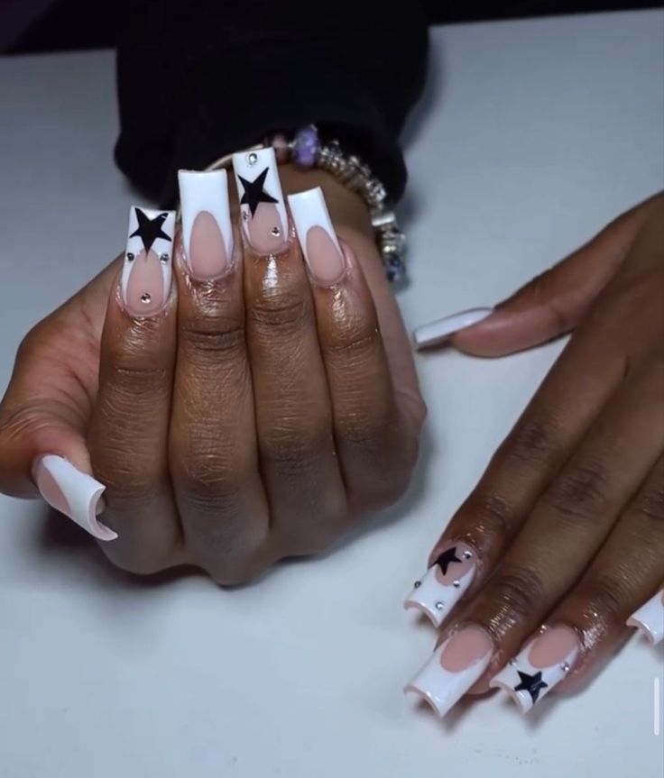 Chic Nail Design: Long Square Tips with Nude Base, Glossy White, Black Stars, and Gem Accents.