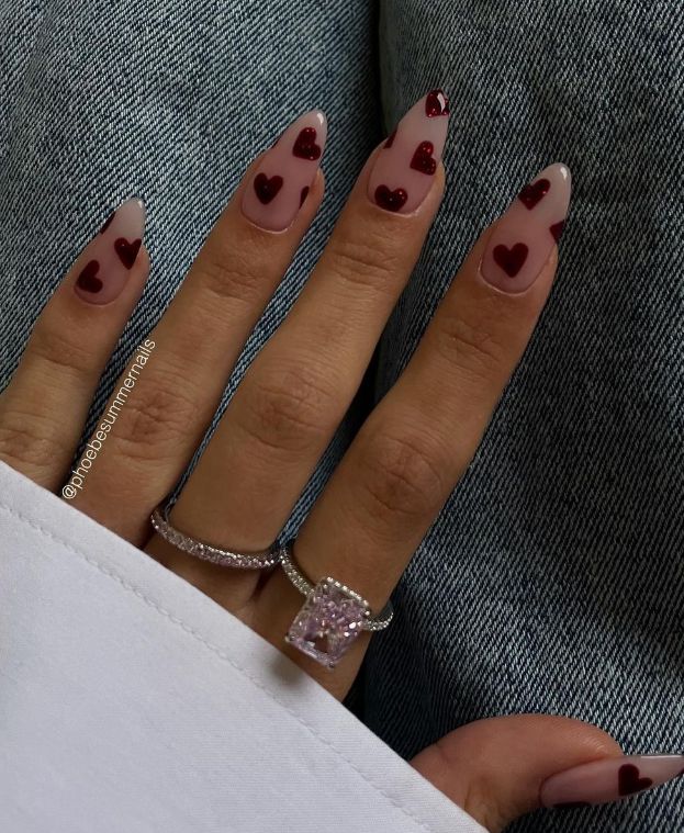 Chic Coffin-Shaped Nails: Nude Base with Bold Deep Red Heart Motifs and Sophisticated Jewelry Accents.