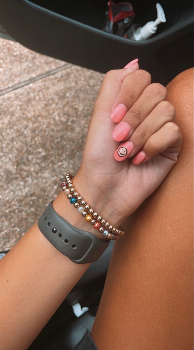 Cheerful Vibrant Pink Nail Design with Playful Smiley Face Accent and Stylish Bracelets.