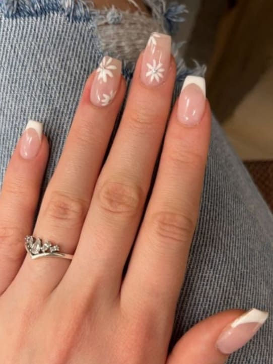 Chic French Tip Nail Design with Delicate White Floral Accents on a Soft Pink Base.