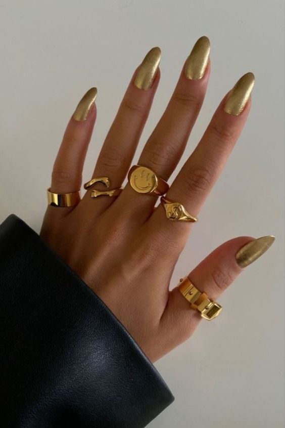 Elegant Golden Almond-Shaped Nails with Glamorous Rings for a Chic Look.