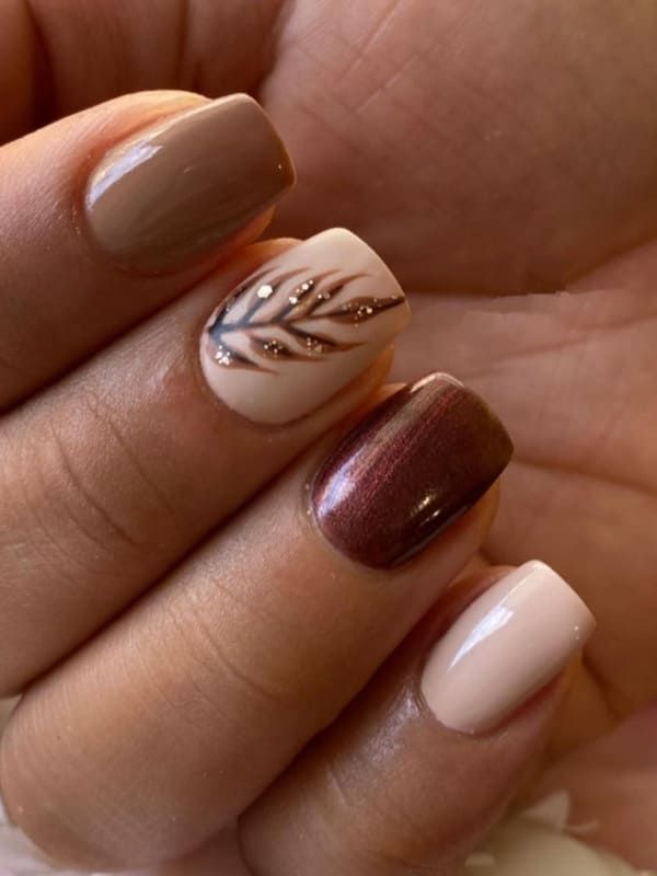 Chic Nail Design: Elegant Neutral and Warm Tones with Intricate Leaf Motifs and Shimmering Accents.