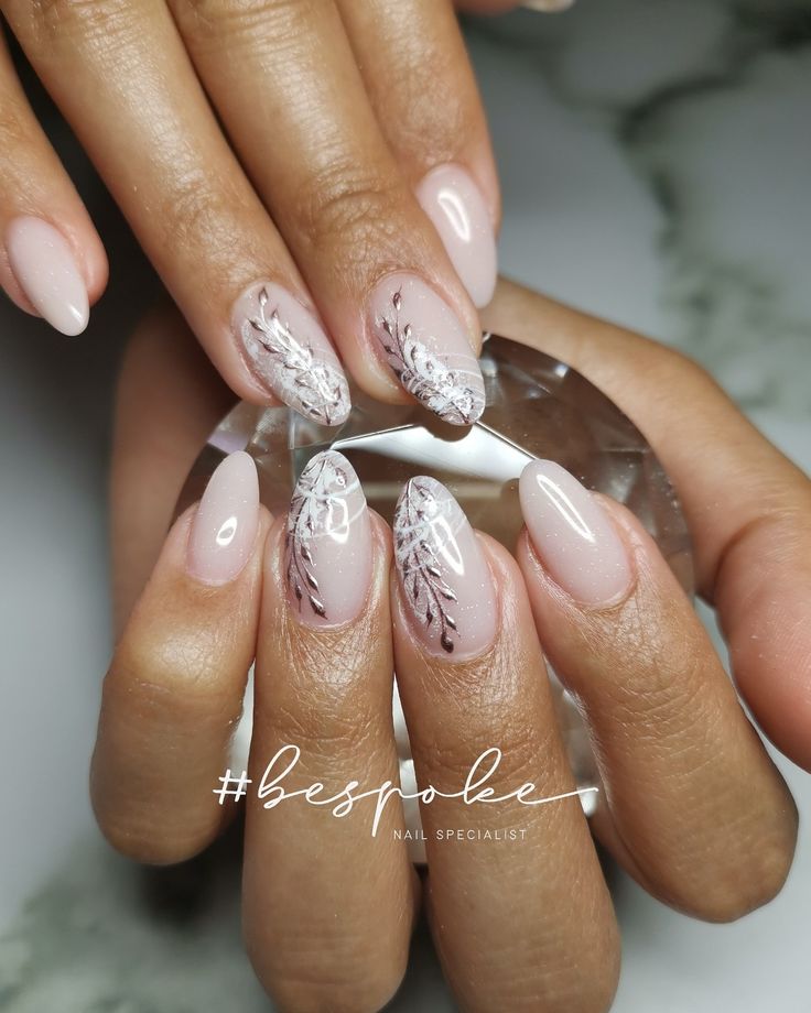 Elegant Nude Nail Design with Intricate White Florals and Metallic Accents.