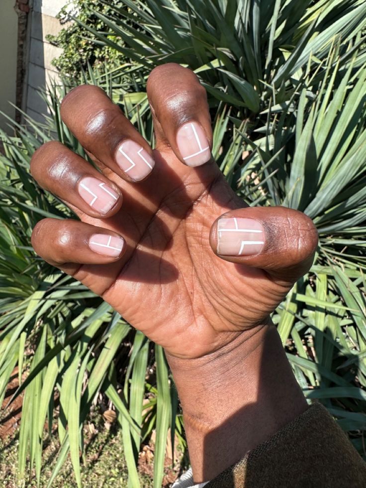 Chic Minimalist Nude Nails with Geometric Lines Amidst Lush Greenery.