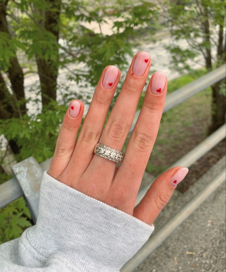 Whimsical Soft Pink Gradient Nail Design with Delicate Red Heart Accents.