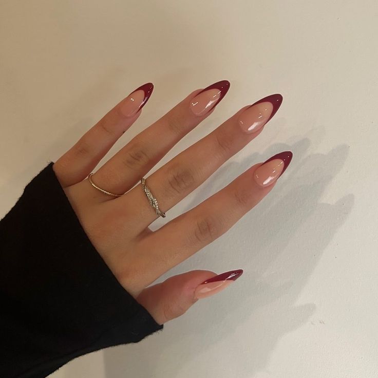 Chic Almond-Shaped Nails with Glossy Nude and Deep Burgundy Tips Enhanced by Subtle Rings.