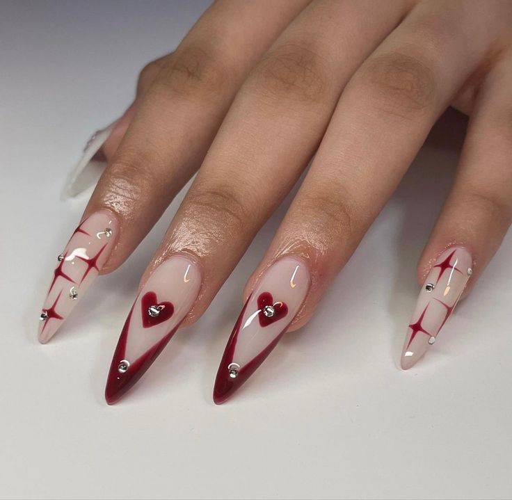 Elegant Heart-Inspired Stiletto Nail Design with Red and Nude Colors, Sparkling Rhinestones, and Star Patterns.