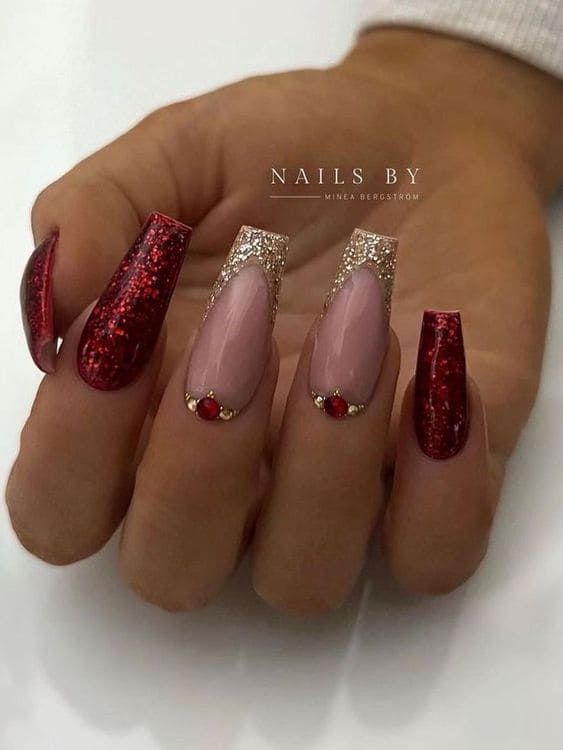 Luxurious Nail Design: Deep Red and Soft Nude with Sparkly Gold Accents and Bold Red Gems