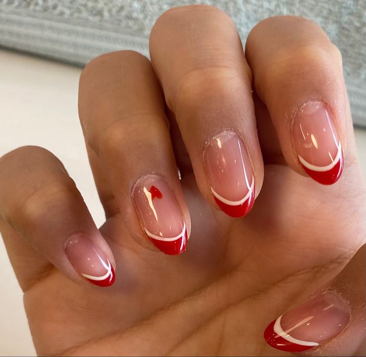 Chic Nail Design: Translucent Base with Vibrant Red French Tips and Elegant Swirls.