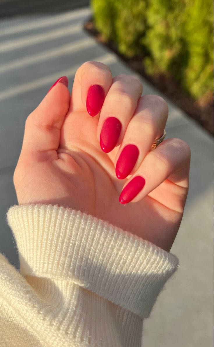 Elegant Almond-Shaped Red Nails Elevate a Neutral Sweater Look with Glamour.