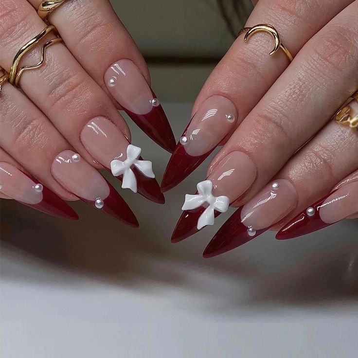 Sophisticated Almond-Shaped Nails: Striking Deep Red Tips with Nude Base, White Bows, and Pearls.