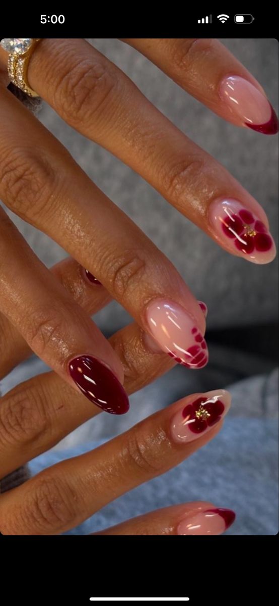 Chic Nail Design: Deep Burgundy Tips with Soft Pink, Nude Bases, Floral Accents, and Gold Embellishments.