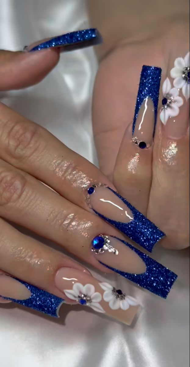 Bold Sparkling Blue Nail Design with Glittery Tips and Floral Accents.