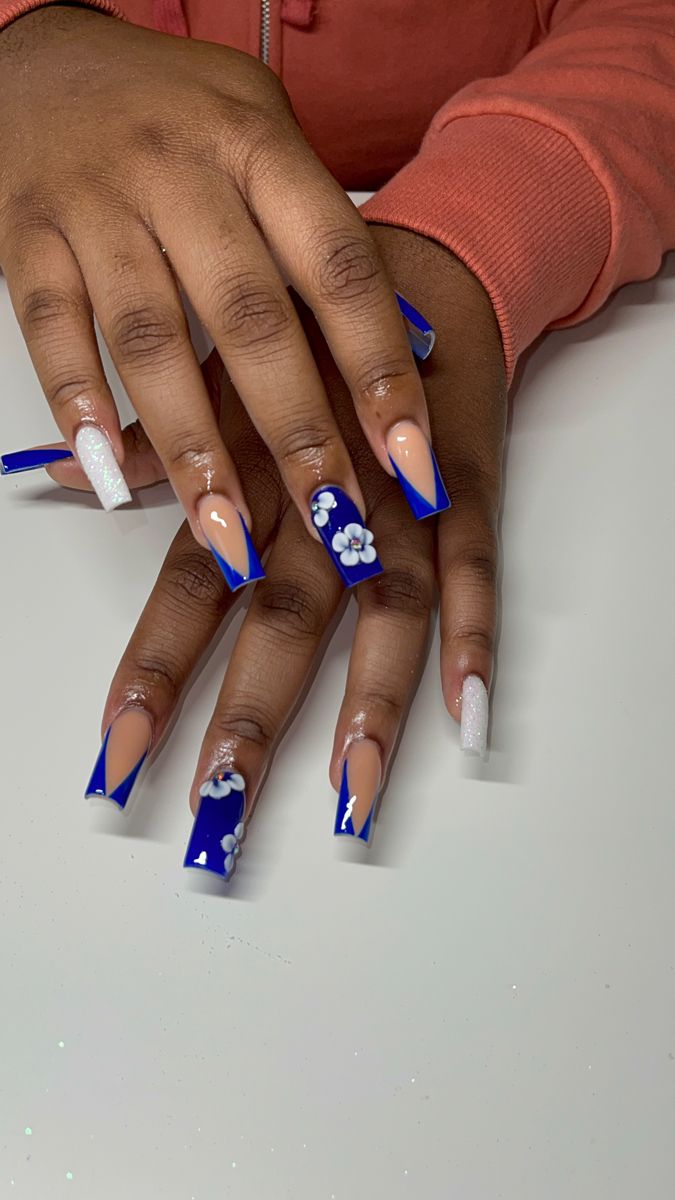 Vibrant Deep Blue and Pastel Nail Design with Floral Accents and Glitter Tips.